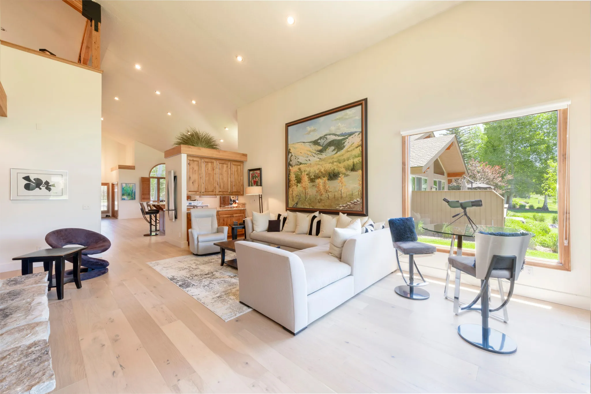 Spacious living area featuring light wood-finish flooring, a vaulted ceiling with recessed lighting, and a prominent picture window