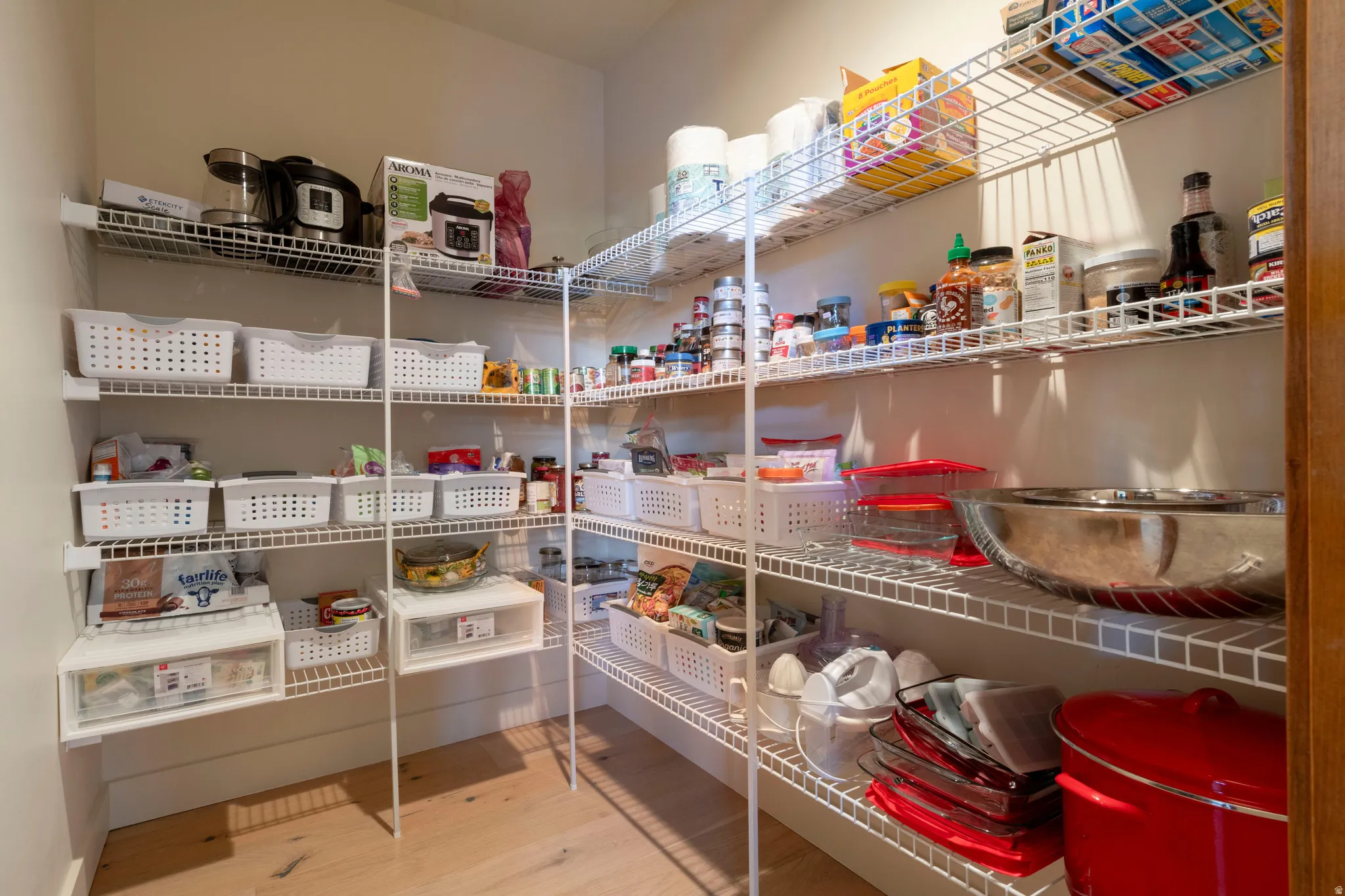 Walk-in pantry featuring extensive wire shelving, natural wood-finish flooring, and bright wall finishes