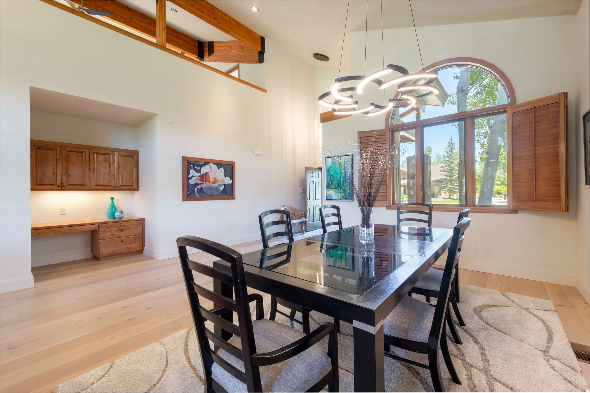 Spacious dining area featuring a prominent arched window with wooden shutters, a contemporary pendant light fixture, and light wood-finish flooring