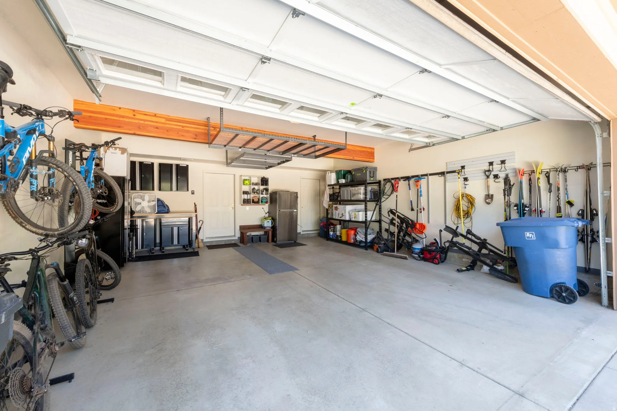 Spacious garage with light-toned concrete flooring, overhead storage racks, integrated wall storage systems, and a dedicated utility sink area