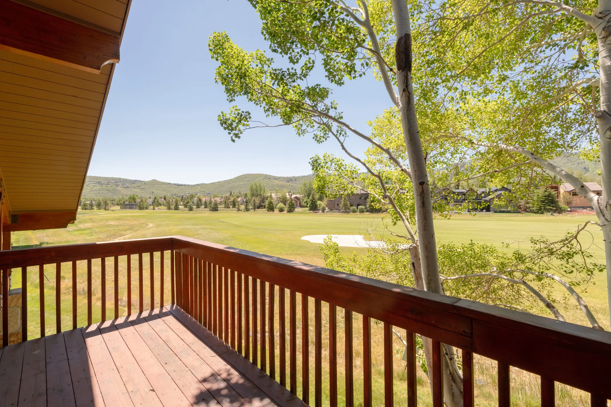 Outdoor deck featuring wood-finish railing and flooring, providing an expansive overlook of a verdant landscape with distant hills and scattered residences