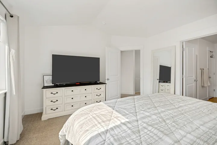 Bright bedroom with a vaulted ceiling, wall-to-wall carpeting, and white walls