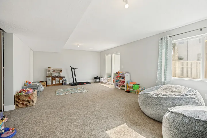 Spacious room featuring light gray walls, plush carpeting, recessed lighting, a sliding glass door, and a large window with white framing