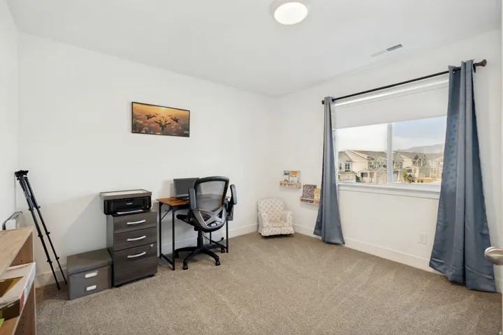 Carpeted room featuring a large window with roller shades and drapery, white walls, and a ceiling-mounted light fixture