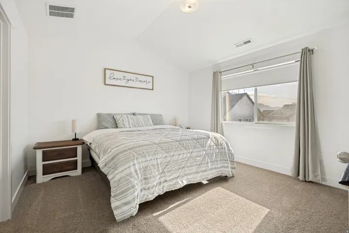 Carpeted interior space featuring a window with roller shade and curtain rods, white walls, and a sloped ceiling
