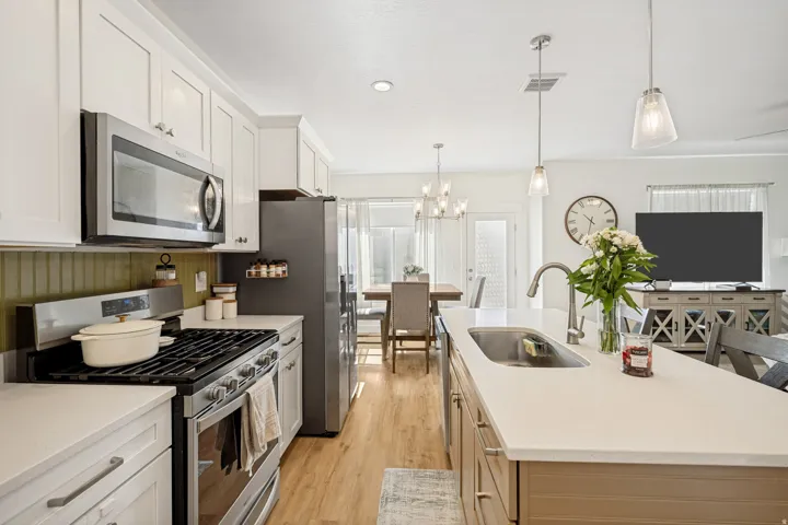 Modern kitchen featuring white shaker cabinetry, stainless steel appliances, light-toned countertops, a central island with an undermount sink, and wood-finish flooring