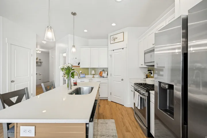 Kitchen featuring a large central island with an undermount sink, pendant lighting, stainless steel appliances, white cabinetry, and wood-finish flooring