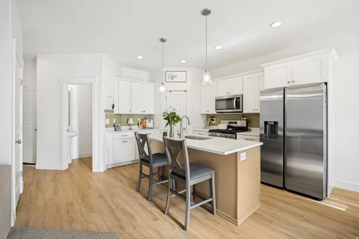 Modern kitchen featuring a central island with seating, stainless steel appliances, white cabinetry, wood-finish flooring, and recessed lighting