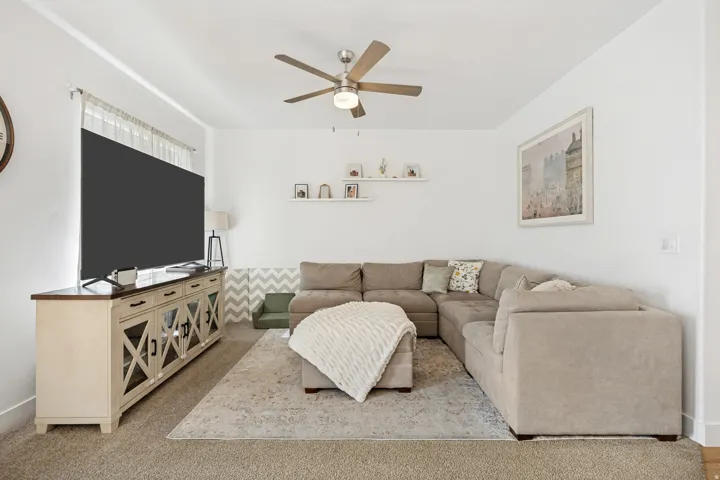 Carpeted living area featuring a ceiling fan with integrated lighting, built-in shelving, and a media console with glass-front cabinetry
