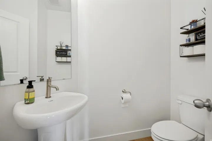 Pedestal sink with a brushed nickel faucet, large wall-mounted mirror, and white toilet