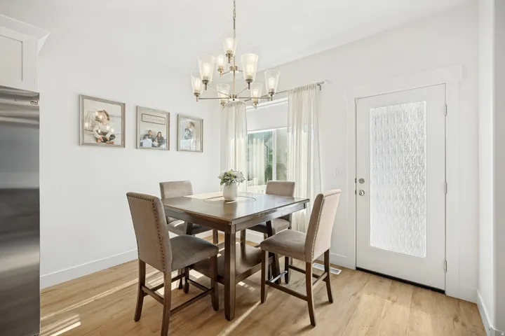 Dining area featuring wood-finish flooring, a contemporary chandelier, and a door with frosted glass panel