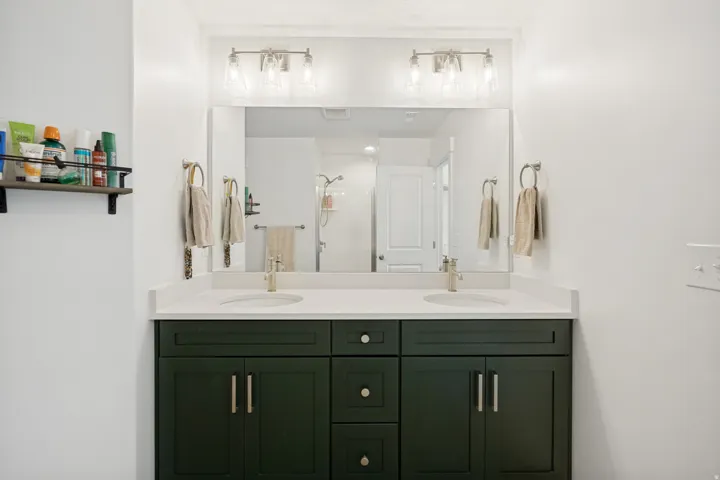 Bathroom vanity featuring dual sinks, a large wall-mounted mirror, and overhead lighting