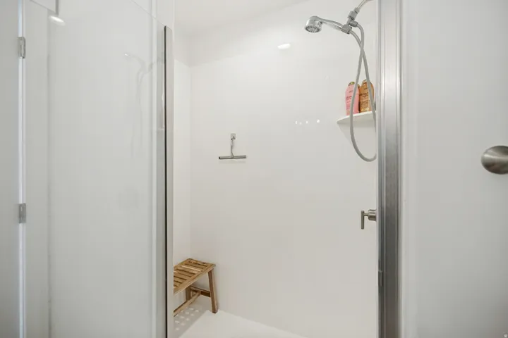 Enclosed shower with clear glass door, white surround, and brushed nickel fixtures