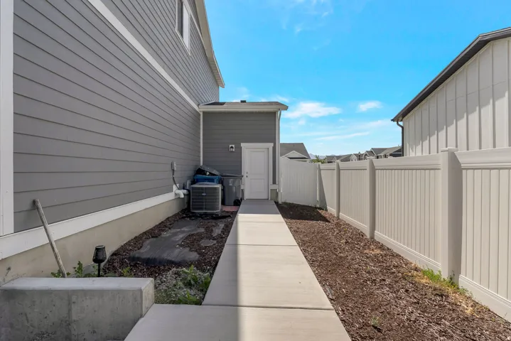 Concrete walkway leading to a service entrance, bordered by a white privacy fence