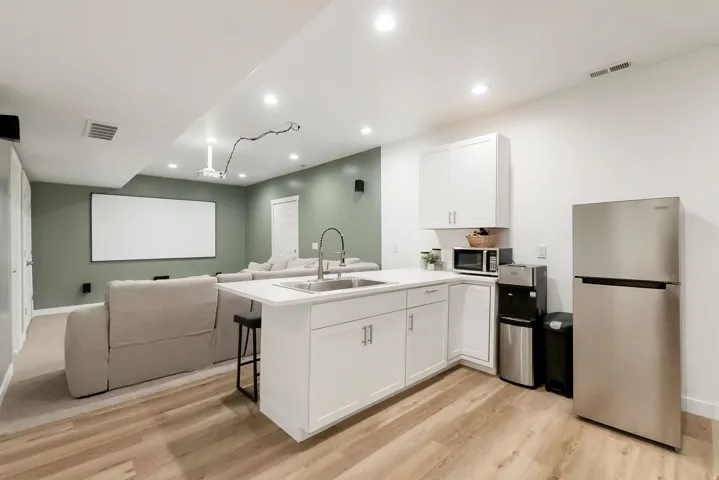 Open-concept entertainment space featuring wood-finish flooring, a white kitchen island with an undermount sink, white cabinetry, and stainless steel appliances
