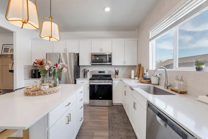 Contemporary kitchen featuring a large central island with a white countertop, white cabinetry with silver hardware, stainless steel appliances, a tile backsplash, and wood-finish flooring