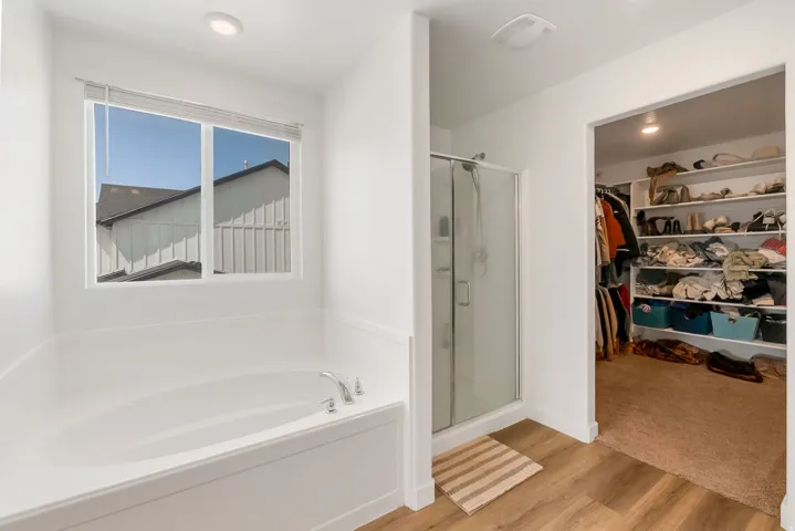 White soaking tub with chrome fixtures, glass-enclosed shower, wood-finish flooring, and a recessed ceiling light