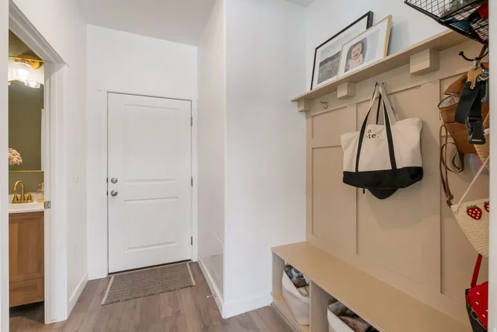 Entryway featuring wood-finish flooring, a white panel door, and a built-in mudroom bench with a shelf and coat hooks