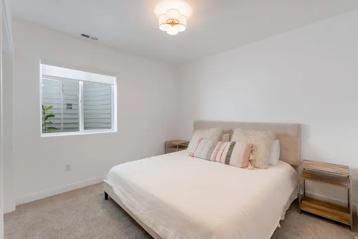Bright room featuring light-colored carpeting, white painted walls, a flush-mount ceiling light fixture, and a window with a window well