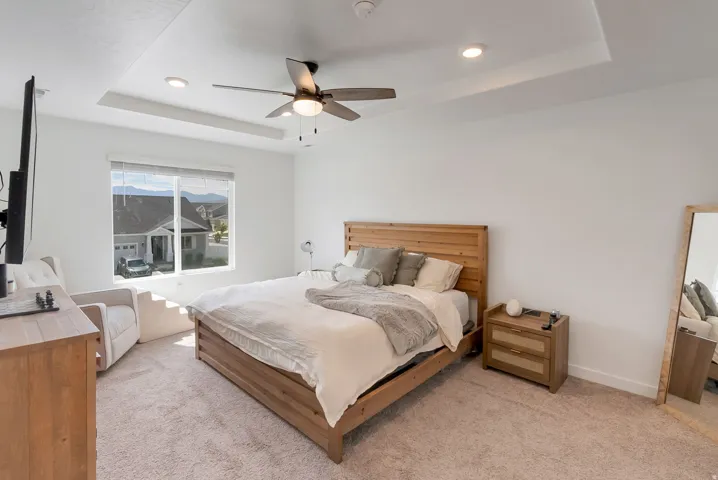 Carpeted room featuring a large window, tray ceiling, recessed lighting, and a ceiling fan