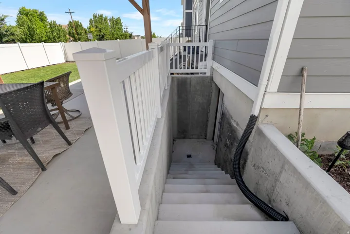 Concrete patio featuring an exterior staircase with white railings, leading to a below-grade entry