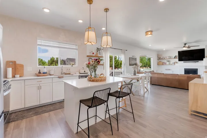 Open-concept kitchen and living area featuring a central island with countertop seating, stainless steel appliances, light wood-finish flooring, and white cabinetry