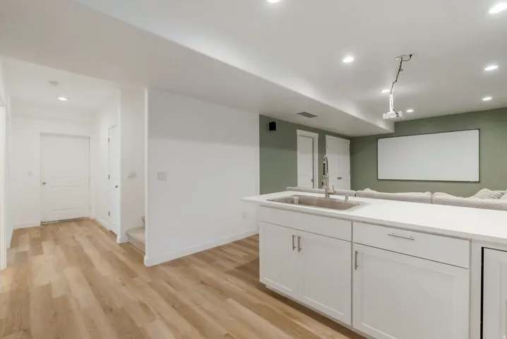 Lower level featuring wood-finish flooring, white cabinetry, a stainless steel sink, and recessed lighting