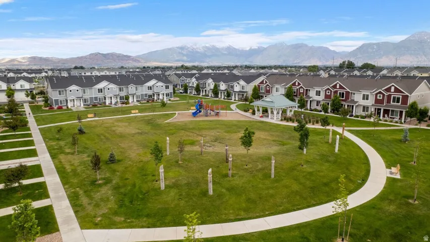 Expansive green space featuring a playground structure, a white gazebo, and walking paths, surrounded by residential townhomes with mountain backdrop