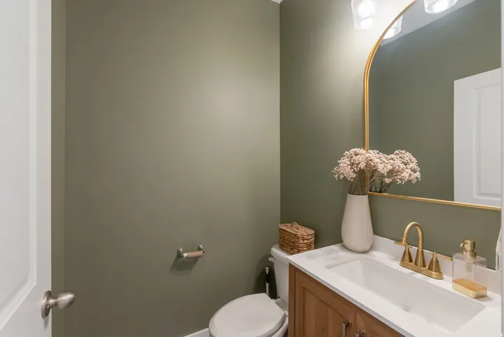 Powder room featuring a gold-framed arched mirror, a gold-finish faucet, and a light wood-finish vanity with a white countertop and integrated sink