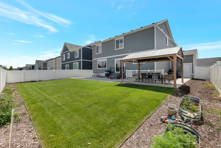Expansive backyard featuring a manicured lawn, white vinyl fencing, concrete patio, and a covered outdoor structure with a metal roof