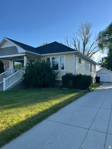 Yellow siding exterior with white trim, dark shingle roof, and a covered porch featuring white railings