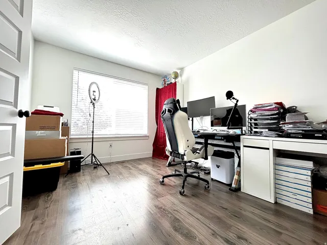 Bright room featuring wood-finish flooring, white walls, and a large window with blinds