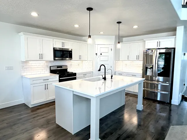 Kitchen featuring a white countertop island with a matte black faucet, white shaker cabinetry, stainless steel appliances, and wood-finish flooring
