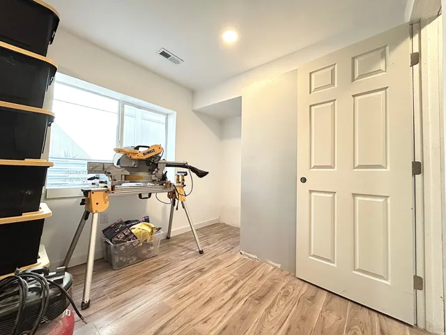 Spacious room featuring wood-finish flooring, a large window, a ceiling-mounted light fixture, and a paneled door