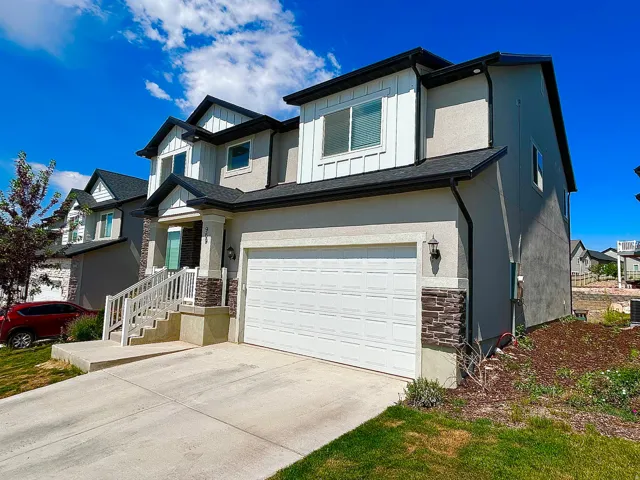 Modern two-story residence featuring a two-car garage, stucco exterior with stone accents, a covered entry with white railings, and dark shingle roofing