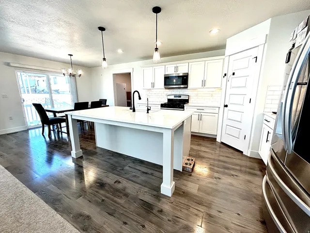 Kitchen featuring a central island with white countertop, white cabinetry with black hardware, subway tile backsplash, stainless steel microwave, and wood-finish flooring