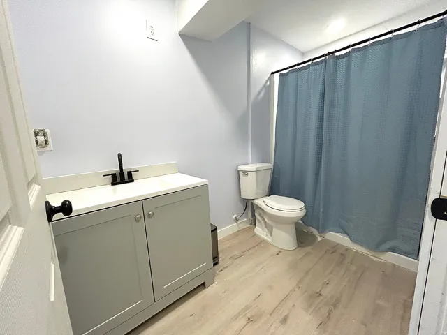 Bathroom featuring a grey vanity with a white countertop, matte black faucet, and wood-finish flooring