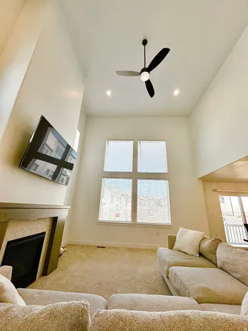 Vaulted ceiling living space featuring a modern fireplace with tile surround, multiple windows, recessed lighting, and a ceiling fan