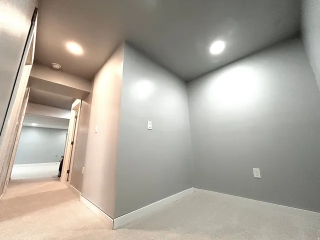Interior hallway with light gray walls and white baseboards, featuring recessed lighting and light-colored carpeting