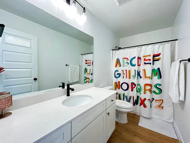 Bathroom featuring a white vanity with an integrated sink, black faucet, a large mirror, and wood-finish flooring