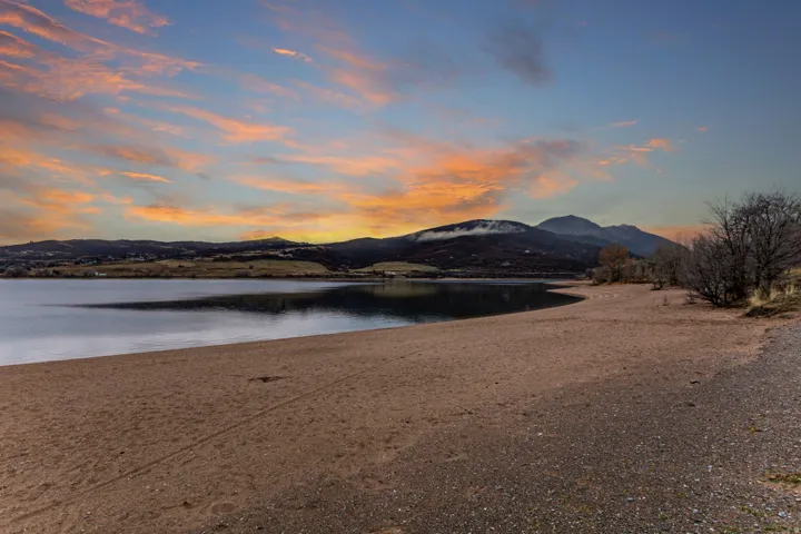 Expansive sandy shoreline bordering a tranquil body of water, with distant mountains providing a natural backdrop