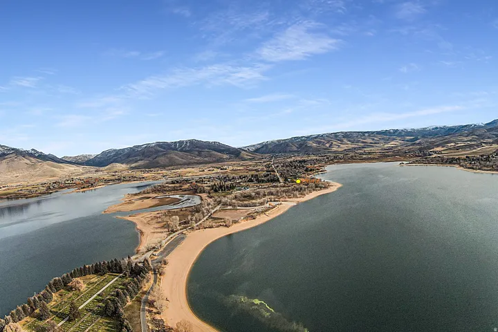 Expansive aerial showcasing a large body of water, surrounded by mountainous terrain and a developing shoreline