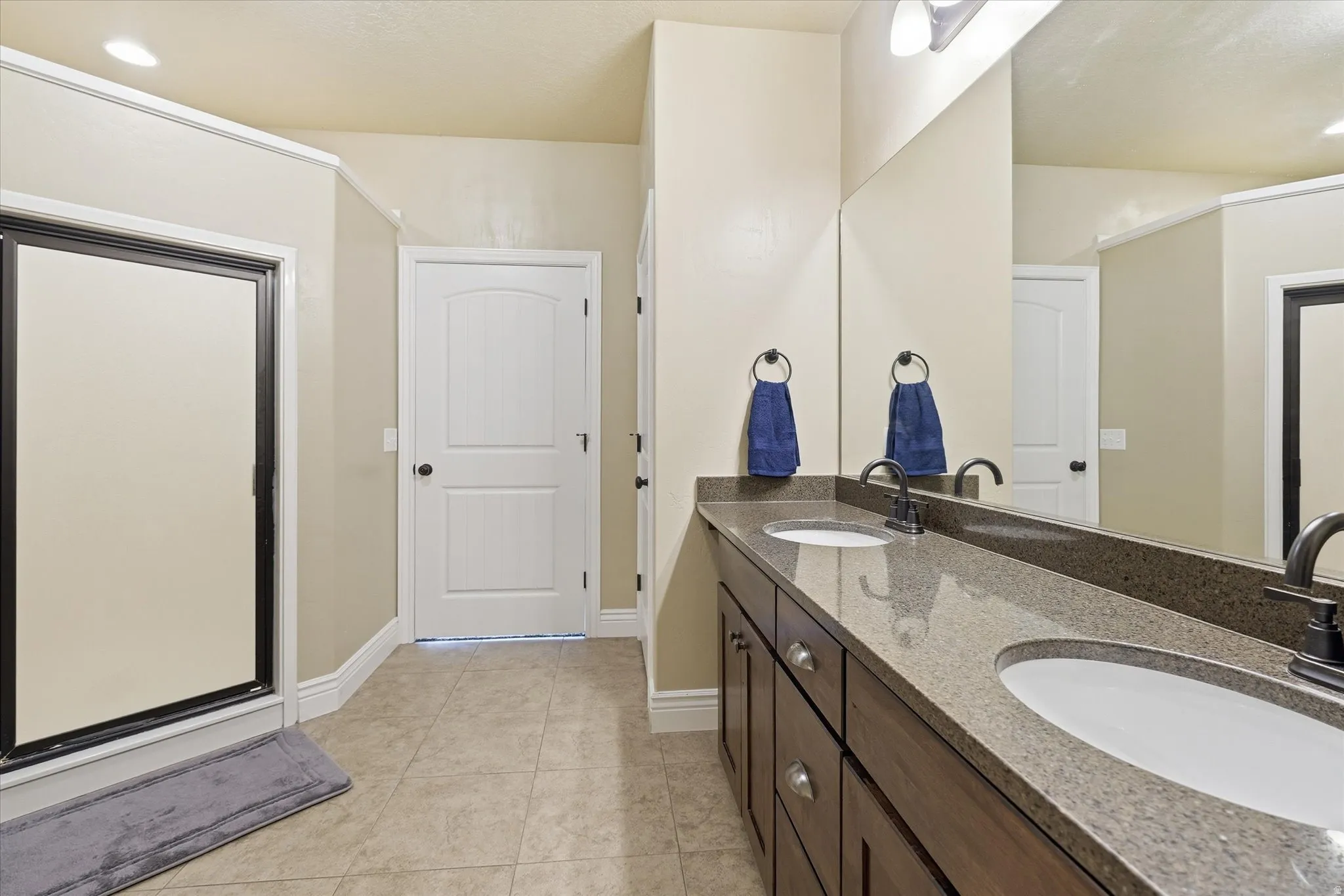Dual vanity with a stone-finish countertop, dark wood-finish cabinetry, and matte black fixtures
