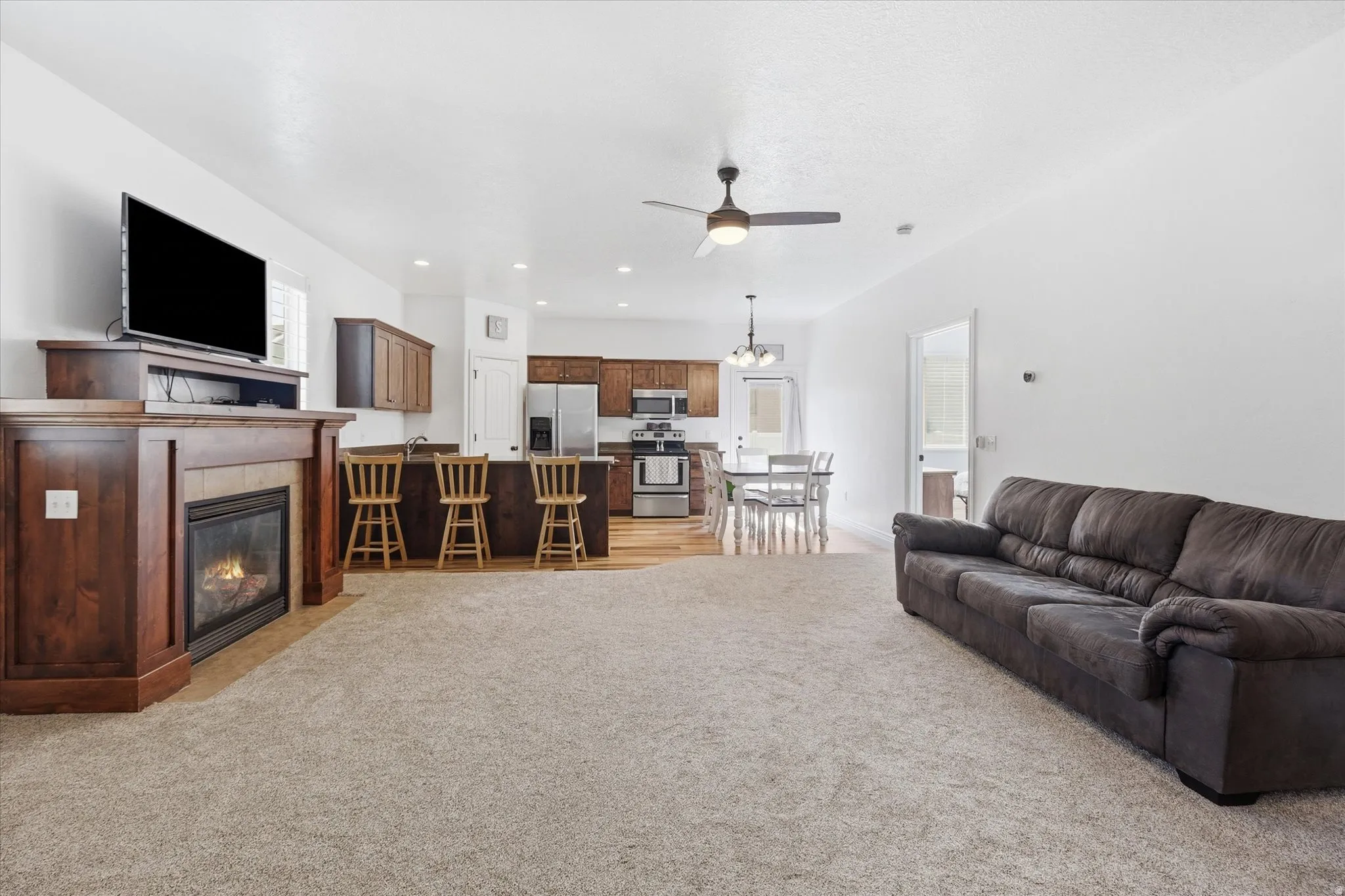 Open-concept living space featuring a built-in fireplace with a wood mantel, a kitchen island with seating, dark wood cabinetry, and stainless steel appliances