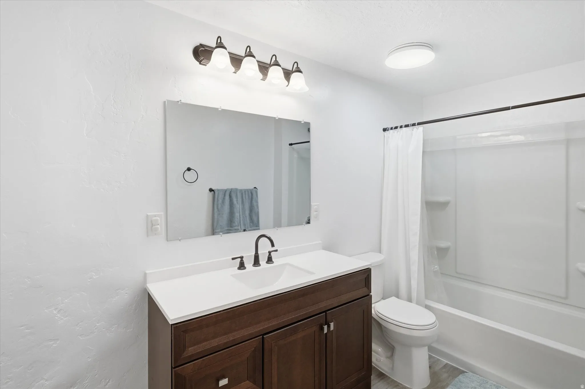 Bathroom featuring a brown wood-finish vanity with a white countertop and integrated sink, framed by a rectangular mirror