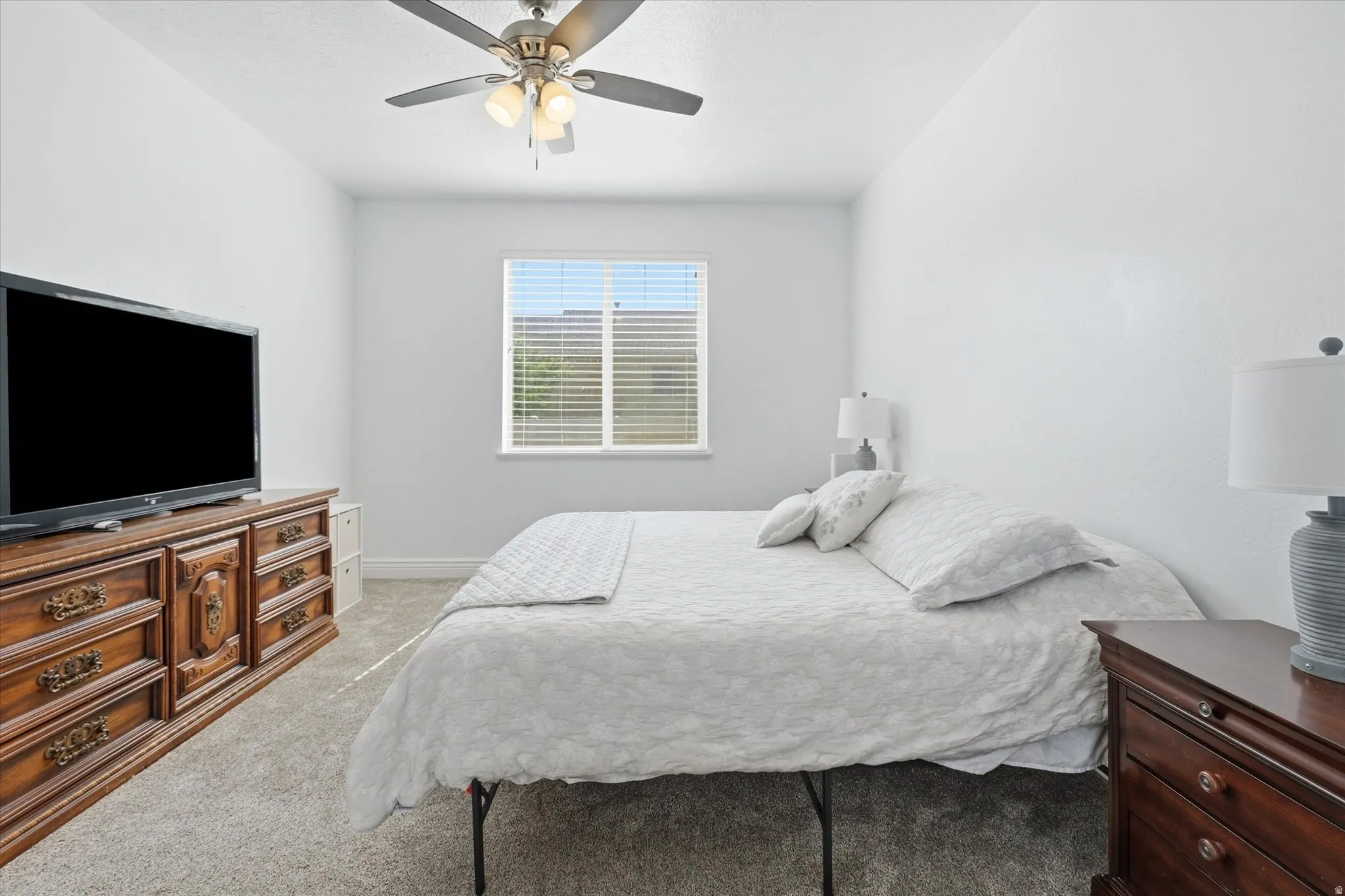 Carpeted interior with light-colored walls, a window featuring blinds, and a ceiling fan with integrated lighting