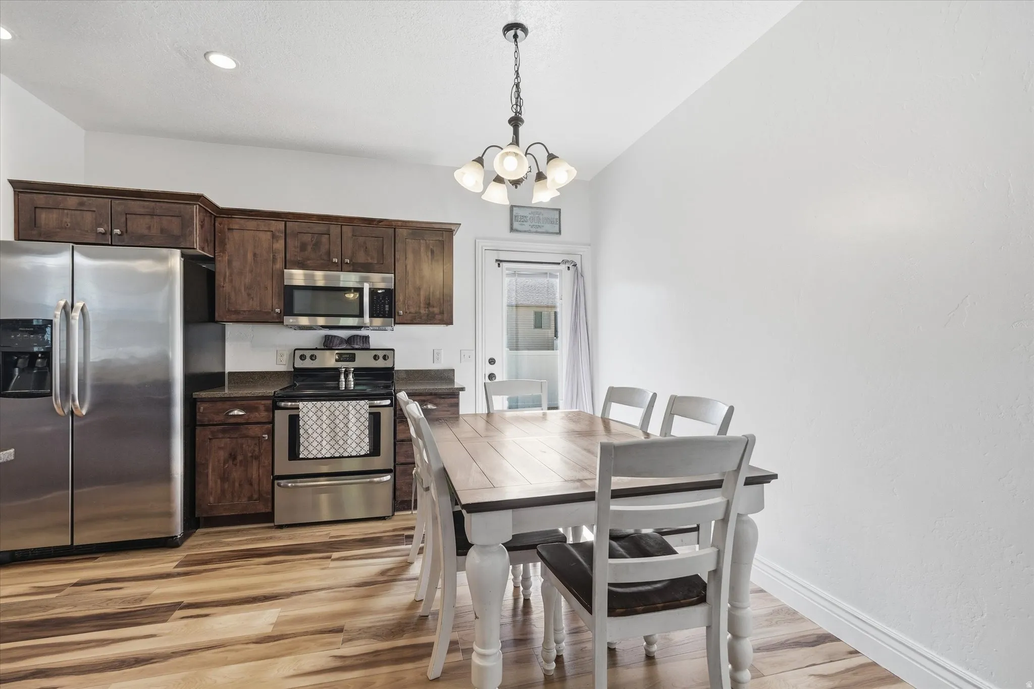 Kitchen and dining area featuring wood-finish flooring, dark wood cabinetry, stainless steel appliances, and recessed lighting