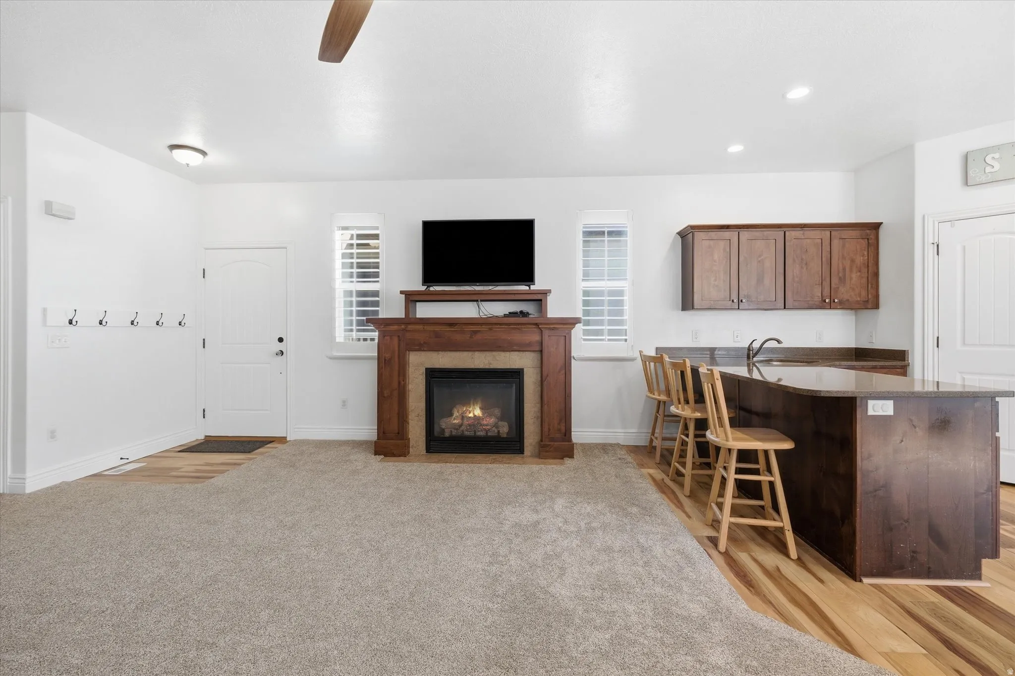 Living area featuring a stone-faced fireplace with wood mantel, ceiling fan, and carpet flooring