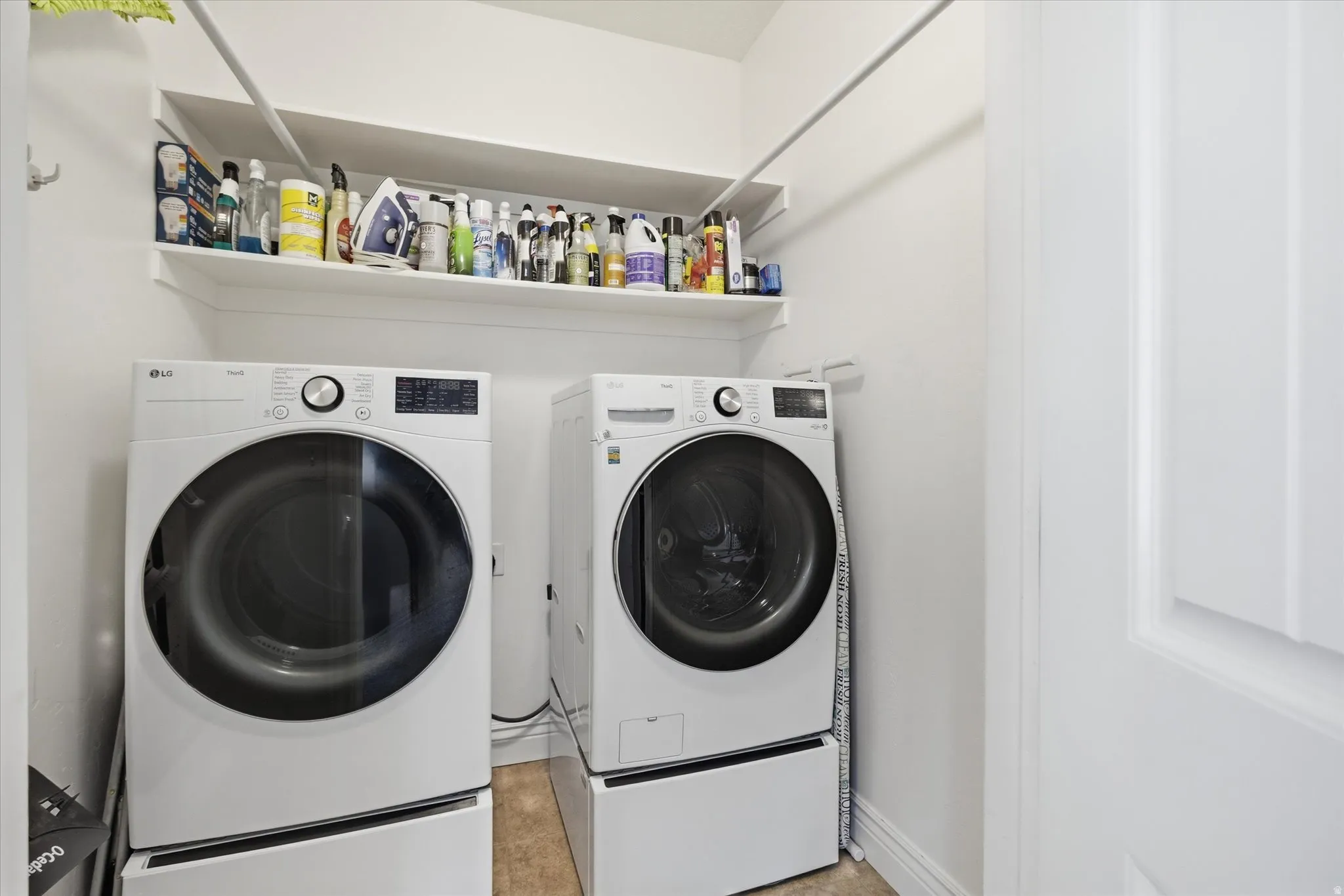 Dedicated laundry area featuring a white floating shelf, white walls, and light-toned flooring