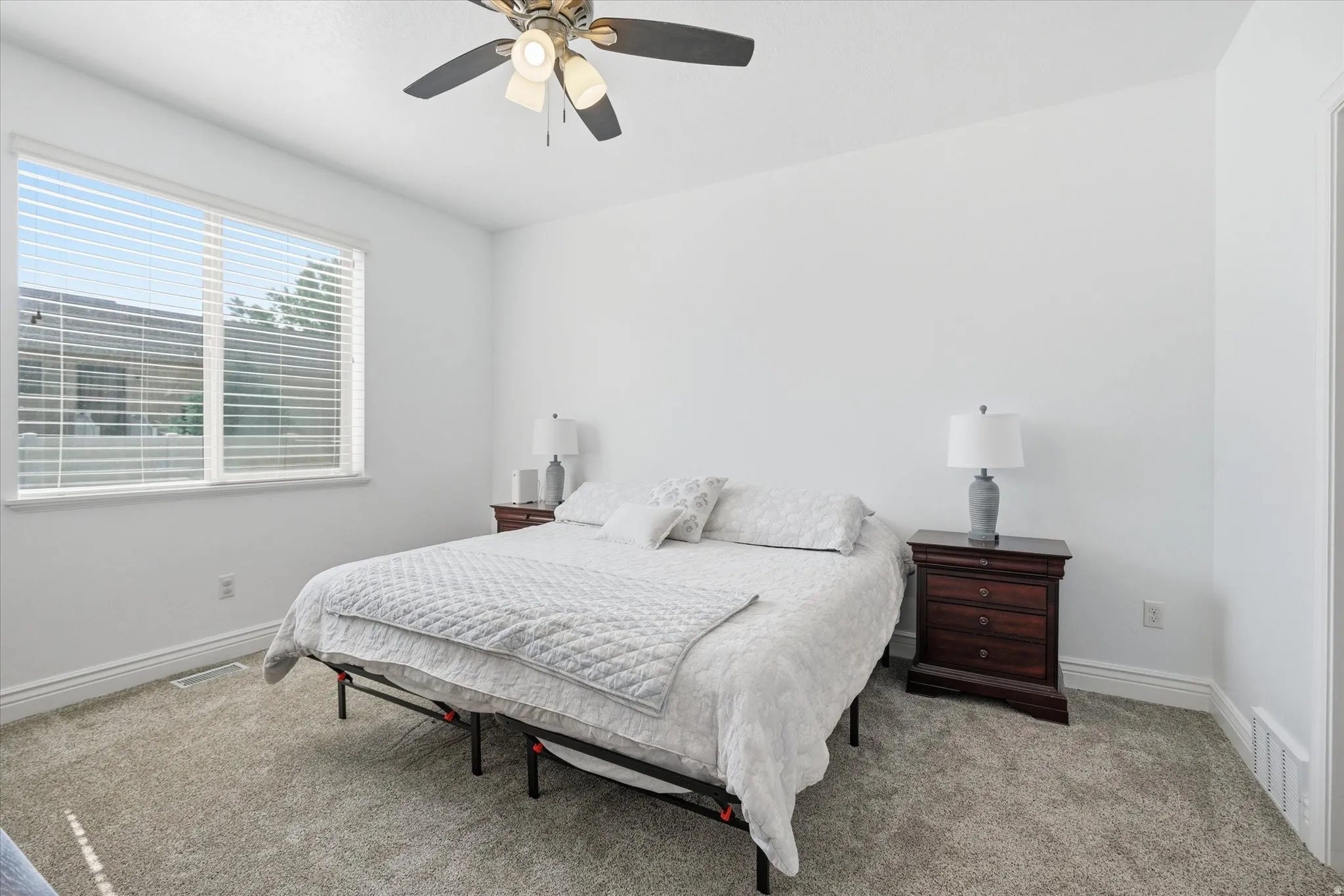 Bright room featuring a large window with blinds, a ceiling fan with integrated lighting, plush carpet flooring, white walls, and white baseboards